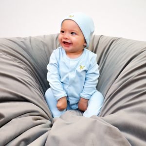 En glad pojke sitter i en ljusblå pyjamas med matchande mössa på en stor grå puff. Pyjamasen är från Lyle & Scott